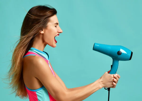Happy young brunette woman with hair dryer on blue mint background — Stock Photo, Image