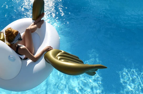 Woman relaxing in luxury swimming pool resort hotel on big inflatable unicorn floating pegasus float — Stock Photo, Image