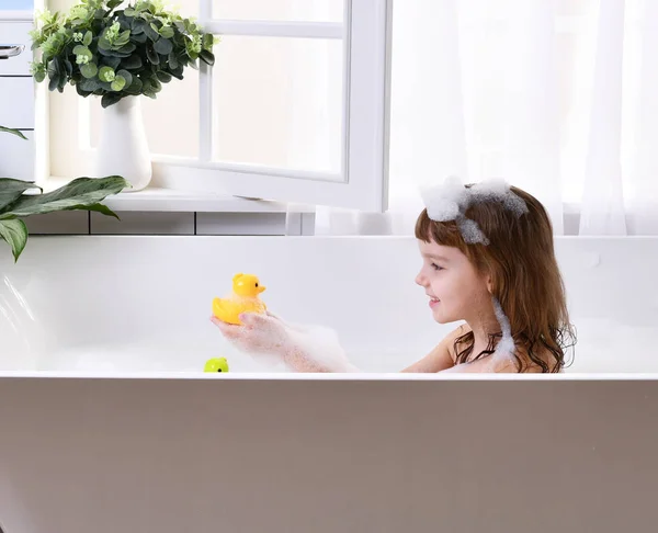 Happy little girl kid sitting in bath tub in the bathroom — стоковое фото
