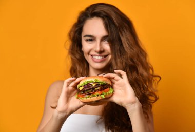 Kadın sarı arka plan üzerinde aç ağız sandviçle hamburger yemek