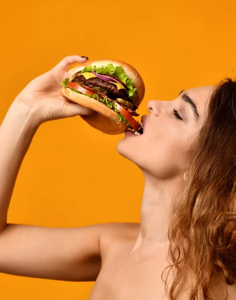 Mujer comer sándwich de hamburguesa con boca hambrienta sobre fondo amarillo — Foto de Stock