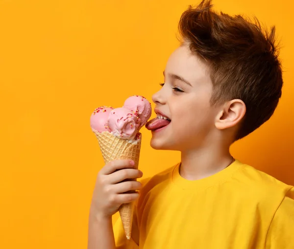 Bebé niño comiendo lamiendo helado de fresa en gofres cono en amarillo —  Fotos de Stock