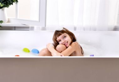 Mutlu küçük bebek kız sarı ördek oyuncak banyoda banyo küvet oyunda oturuyor