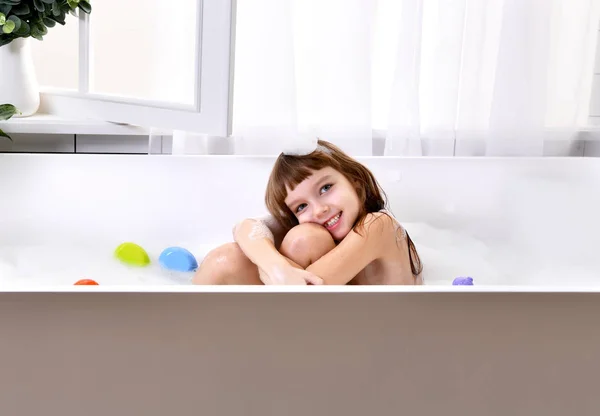 Feliz niña sentada en la bañera jugar con el pato amarillo juguete en el baño — Foto de Stock