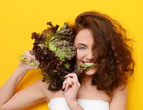 Jolie femme bouclée cheveux manger salade de laitue en regardant le coin sur fond jaune — Photo