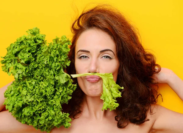 Jolie femme bouclée cheveux manger salade de laitue en regardant le coin sur fond jaune — Photo