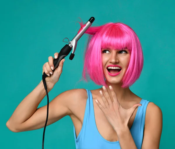 Mujer feliz en peluca rosa con rizador de pelo de hierro de cerámica varita rizadora profesional sobre fondo de menta azul —  Fotos de Stock