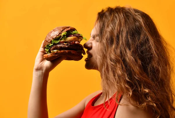 Mulher come sanduíche de hambúrguer com boca faminta no fundo amarelo — Fotografia de Stock