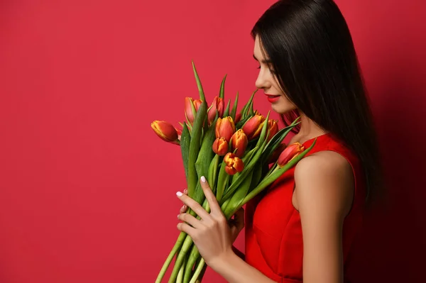 Beautiful woman with bouquet of tulip flowers in red dress and looking at the corner with empty text copy space — Stock Photo, Image