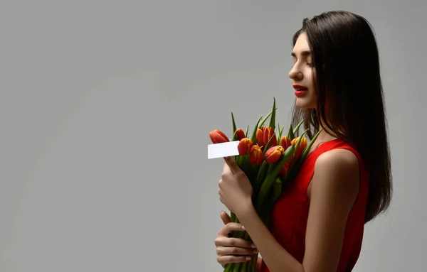 Wanita cantik dengan karangan bunga tulip dengan gaun merah dan stiker kecil di atas tulip dengan ruang teks kosong gratis — Stok Foto
