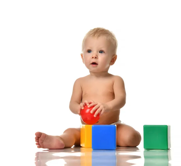 Малыш сидит голый в подгузнике с зелено-голубой кирпичной игрушкой и красным мячом — стоковое фото