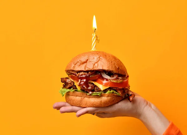 Las manos de la mujer sostienen el sándwich grande de la barbacoa de la hamburguesa con la carne de res y la vela encendida para la fiesta de cumpleaños en amarillo — Foto de Stock