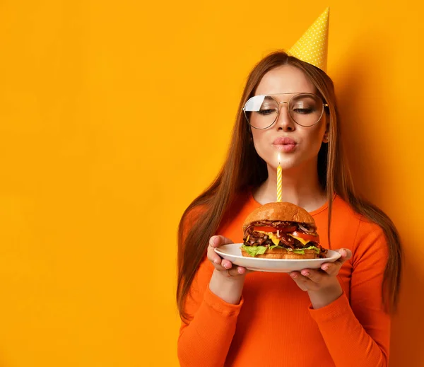 Les mains de la femme tiennent un gros sandwich burger barbecue avec bœuf et bougie allumée pour la fête d'anniversaire sur jaune — Photo