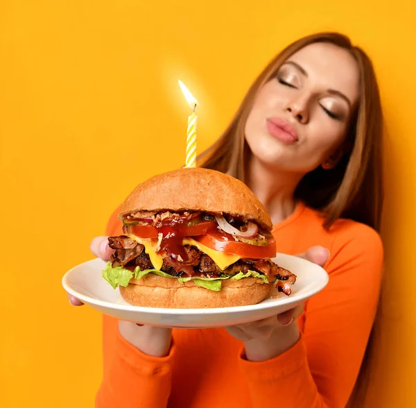 Woman hands hold big burger barbeque sandwich with beef and lit candle for birthday party on yellow Stock Image