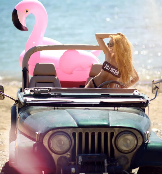 선글라스 화창한 여름 날 거 대 한 팽창 식 거 대 한 분홍색 홍학 float 매트리스와 함께 바다 해변 근처에 비치 트럭 자동차에 앉아 있는 어린 소녀 — 스톡 사진