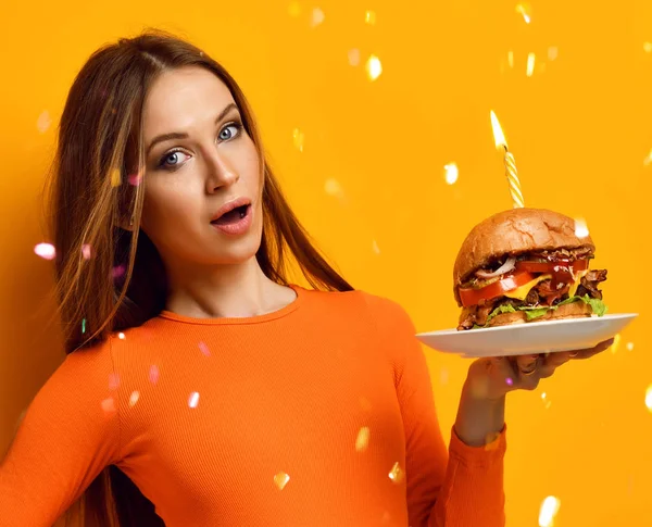 Vrouw handen houden grote hamburger barbecue sandwich met rundvlees en stak kaars voor verjaardagsfeestje op geel — Stockfoto