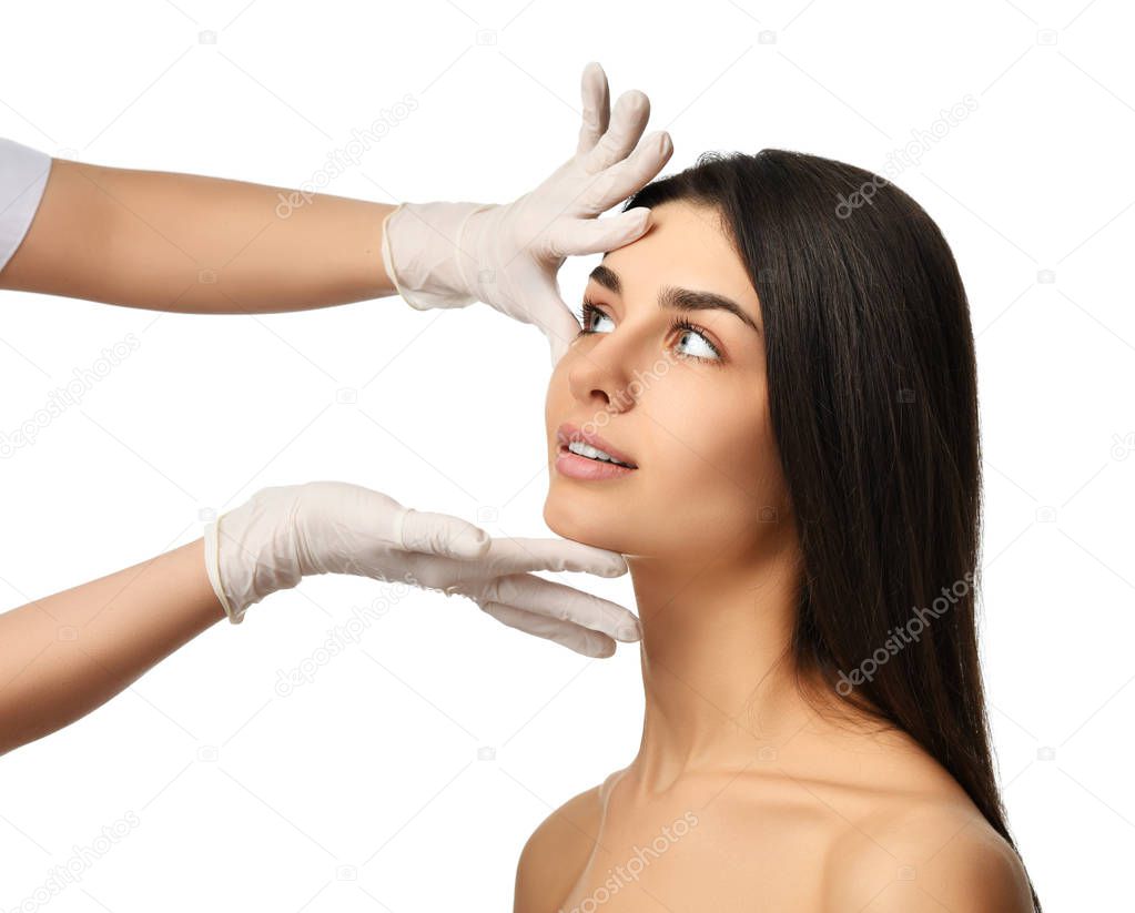 Doctor hands in medical gloves touch beautiful young woman face with closed eyes after plastic surgery 