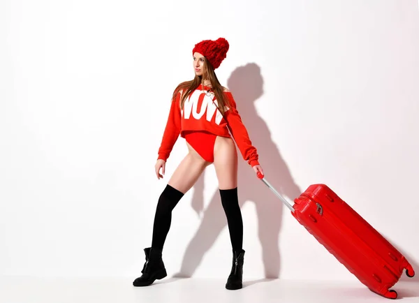 Junge sexy Frau in modischem rotem Körpertuch und Hut mit Reisegepäcktasche auf weißem Grund — Stockfoto