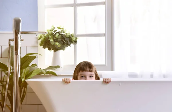 Glad liten baby flicka sitter i badkaret leker med anka leksaker i badrummet — Stockfoto
