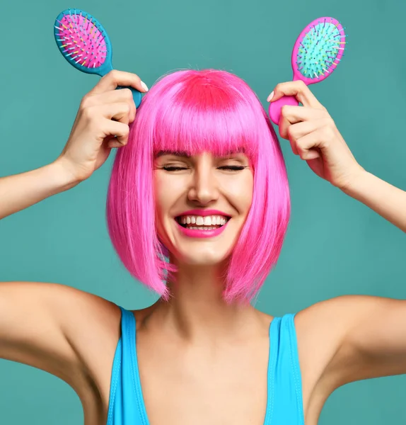 Closeup retrato de moda feliz morena mulher segurar dois pequeno rosa azul escova pente de cabelo pequeno em peruca rosa — Fotografia de Stock