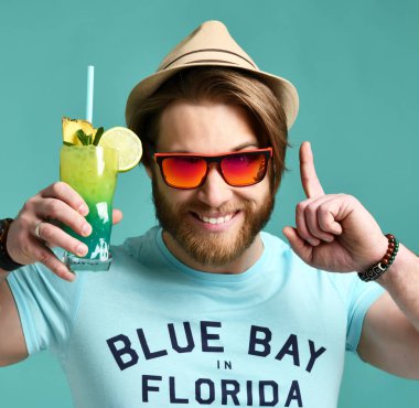 Kırmızı güneş gözlüğü ve şapka genç adam tutun margarita kokteyl içki suyu mutlu alkış mavi üzerinde parmak işaret