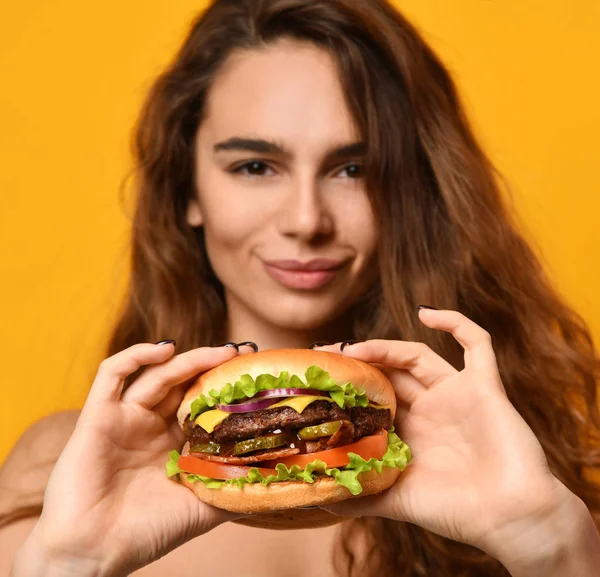Женщина ест сэндвич с бургером с голодным ртом на желтом фоне — стоковое фото