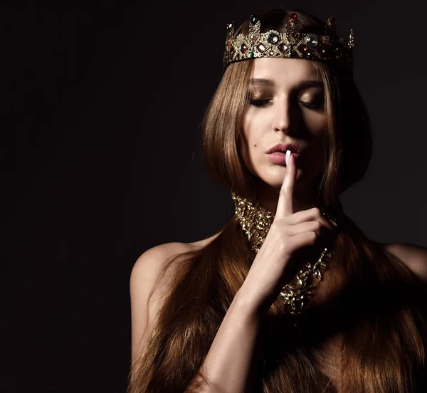 Mooie sexy brunette schoonheid vrouw met lang haar dragen gouden kroon en juwelen tsss ziekteverschijnsel vertonen op donker — Stockfoto