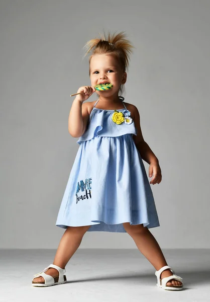 Jeune jolie tout-petit fille enfant avec de gros bonbons sucette sucrée en robe bleue sur gris — Photo