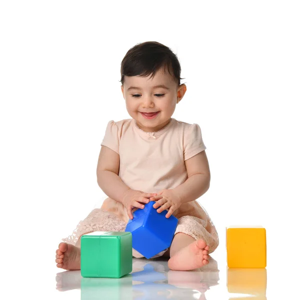 Enfant bébé tout-petit assis en robe avec jouet en brique verte bleue et jaune jouant isolé sur un blanc — Photo