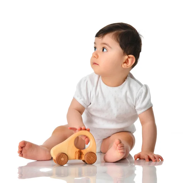 Девятимесячный младенец девочка малышка сидит в белой рубашке с деревянной игрушкой автомобиля — стоковое фото