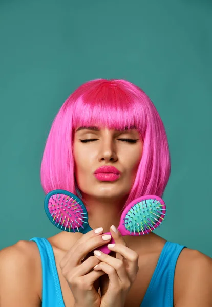 Closeup portrait of happy fashion brunette woman hold two small pink blue yellow small hair comb brush kissing sign in pink wig — Stock Photo, Image