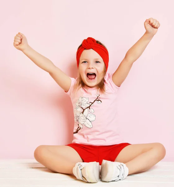 Lindo bebé niña en pijama rosa claro y diadema roja con las manos levantadas —  Fotos de Stock