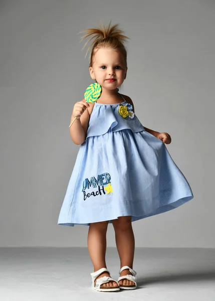 Young pretty toddler girl kid with big  sweet lollypop candy in blue dress on grey — Stock Photo, Image
