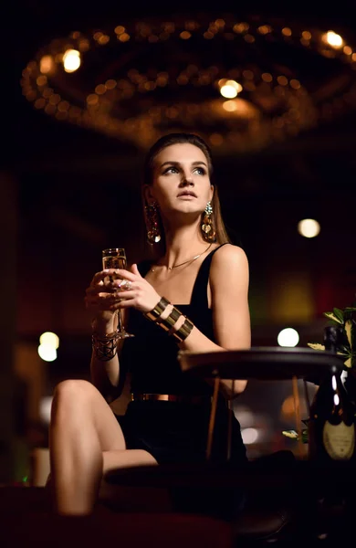 Beautiful sexy fashion brunette woman in expensive interior restaurant drinking champagne waiting on dark cafe — Stock Photo, Image