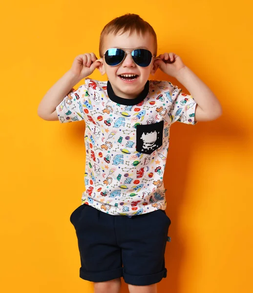 Przedszkola chłopiec dziecko stojąc w niebieskie okulary przeciwsłoneczne i szczęśliwy uśmiechający się na żółty t-shirt — Zdjęcie stockowe
