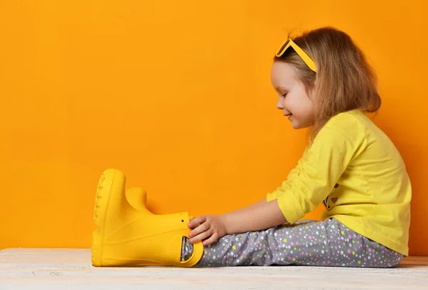Güneş gözlüğü ve t-shirt sarı üzerinde oturan genç çocuk bebek kız çocukta sarı lastik çizmeler — Stok fotoğraf