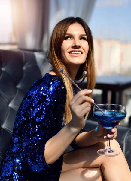 Fashion brunette woman sitting in expensive interior restaurant drinking drinking blue margarita cocktail looking at the corner — Stock Photo, Image