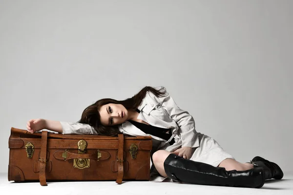 Mulher hipster morena bonita em jaqueta de outono cinza deitada no saco de viagem retro marrom de couro no cinza — Fotografia de Stock