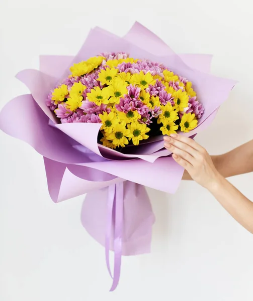 美しい女性手が白地菊の花の花束を黄色と紫に保持します。 — ストック写真