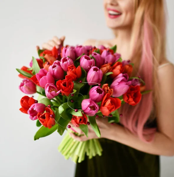 美しい女性が幸せな笑顔灰色の赤とピンクのチューリップの花の花束を保持します。 — ストック写真