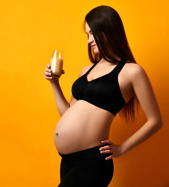 Junge schwangere glückliche Mutter Frau glücklich lächelnd Orangensaft trinken auf gelb — Stockfoto