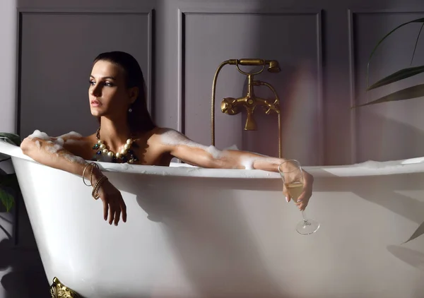 高価な浴槽お風呂酒にシャンパンの浴室を見て角に座っている若い美しい女性 — ストック写真