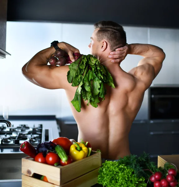 Muskulöser Sportler, der in der Küche steht und Gemüse einkauft, Rettich in der Hand hält und lächelnd in die Ecke schaut — Stockfoto