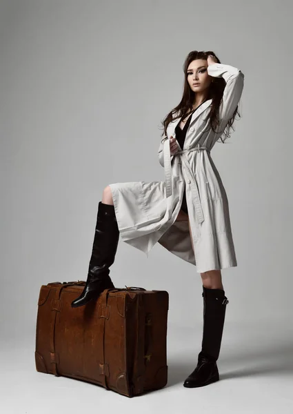 Vackra brunett hipster kvinna i grå höst jacka med blåsiga hår sitter nära läder brun retro travel bag — Stockfoto