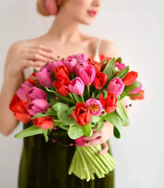 美しい女性はグレーに赤ピンクのチューリップの花の花束を保持します。 — ストック写真