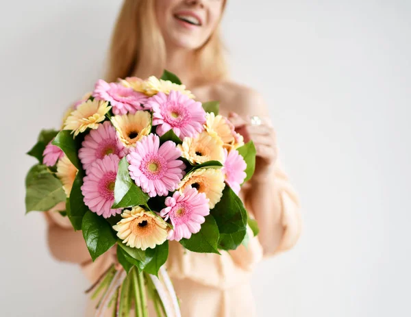 美しい女性が幸せな笑顔灰色のガーベラの花のピンクと黄色の花束を保持します。 — ストック写真