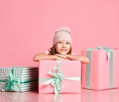 Küçük kız hediye kutularının arkasında oturuyor. İçinde ne olduğunu tahmin etmeye çalışıyor. Pembenin üstündeki fotokopi odasına bakıyor.