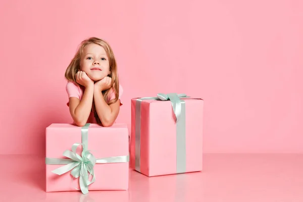 Navidad y Año Nuevo. Chica bonita está sentada detrás de los regalos con la barbilla en las manos, mirando directamente en la cámara en rosa — Foto de Stock