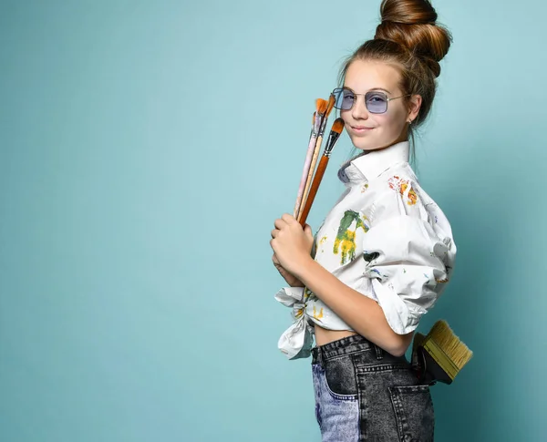 Vrolijke glimlachende jonge vrouw in wit shirt met verf vlekken met een set borstels en een in de achterzak van haar jeans — Stockfoto