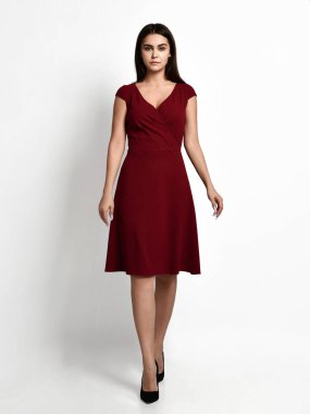 Yeni moda kırmızı kış elbisesi içinde poz veren genç, güzel bir kadın mutlu bir gülümseme içinde beyaz bedenin üzerinde yürüyor.